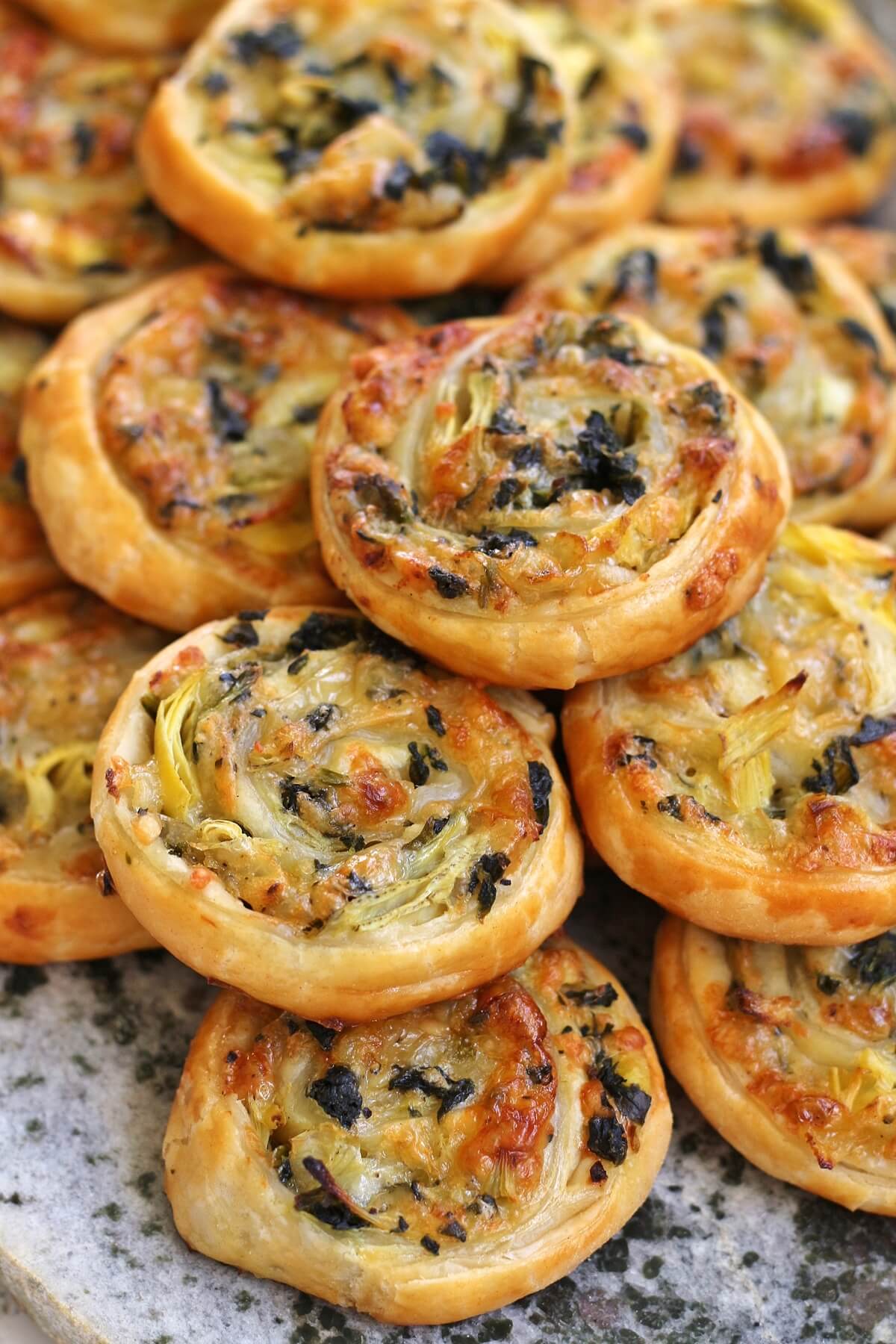 Closeup of golden brown spinach and artichoke puff pastry pinwheels on a stone surface.