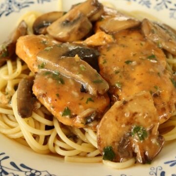 chicken marsala on top of spaghetti in a shallow white bowl with blue decorations