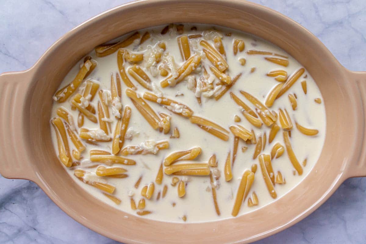 An oval baking dish of pasta mixed with cream and cheeses before baking.