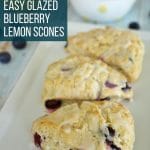 3 blueberry lemon scones on a rectangular white plate with spilled blueberries on the table