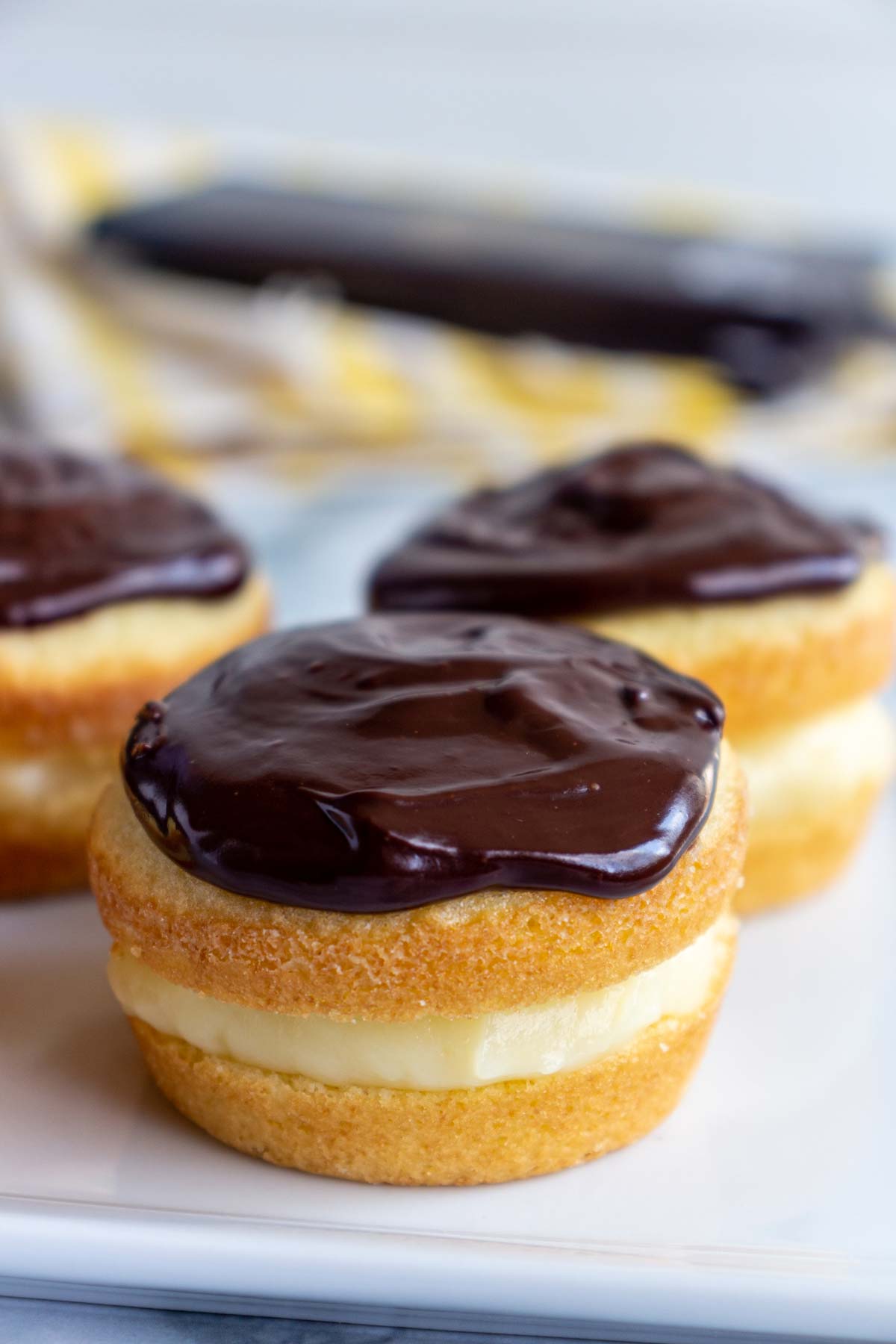 Closeup of Boston cream pie cupcakes with shiny chocolate ganache on top on a white plate.