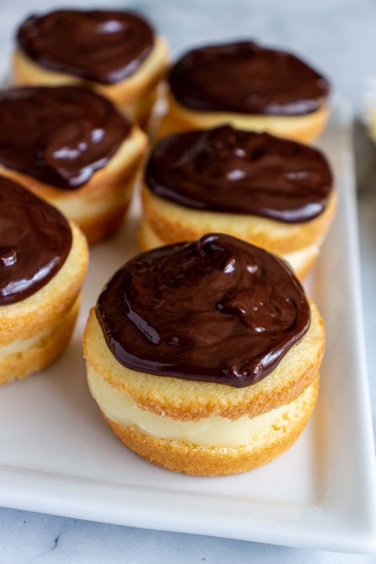 Six Boston cream pie cupcakes arranged in two rows on a white rectangular plate.