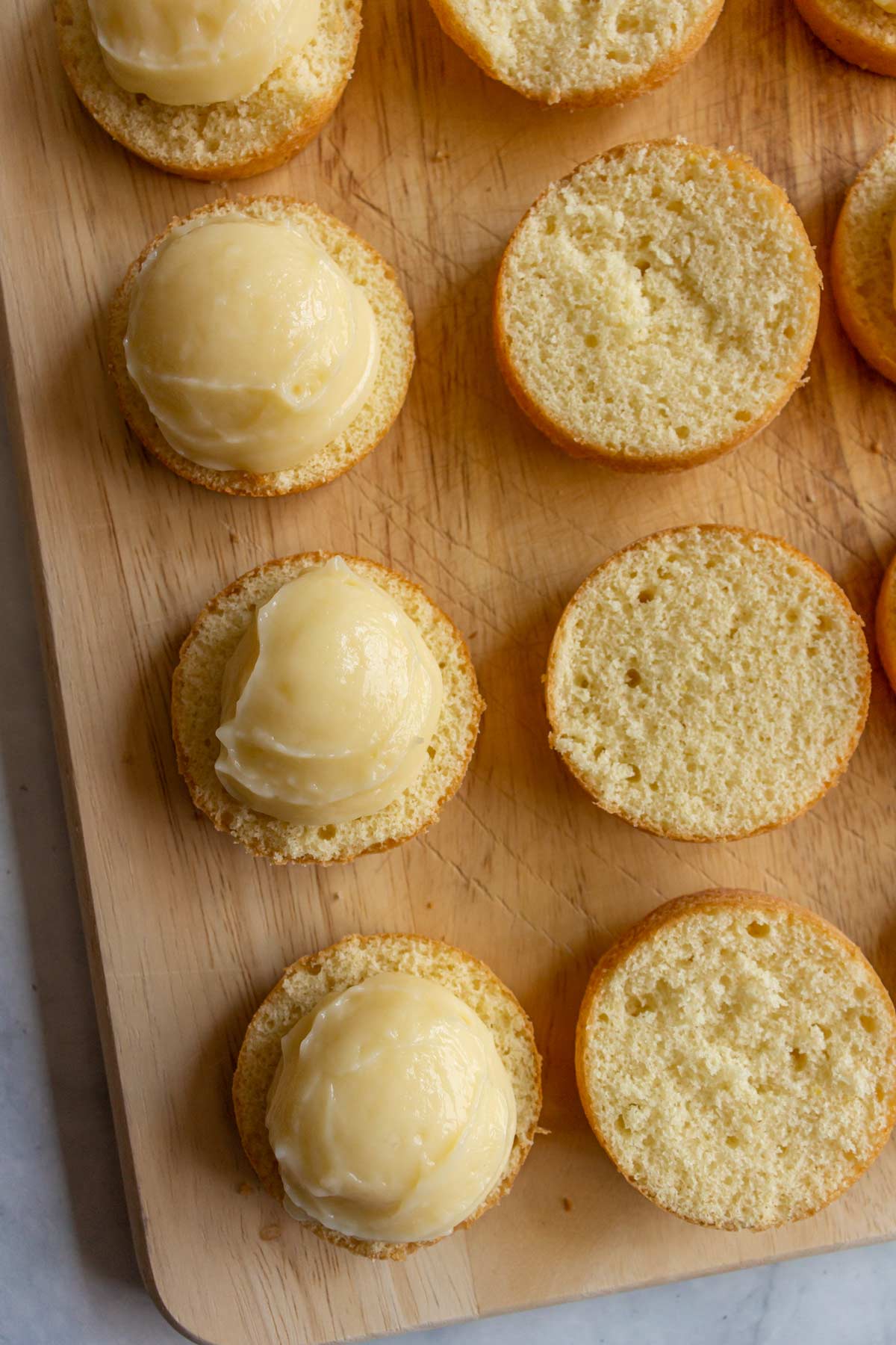 Closeup of halved white cupcakes topped with scoops of pastry cream on a wooden board.