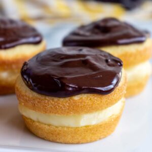 Closeup of Boston cream pie cupcakes with shiny chocolate ganache on top on a white plate.