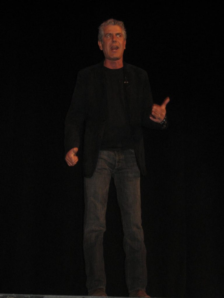 Anthony Bourdain standing in front of a dark background