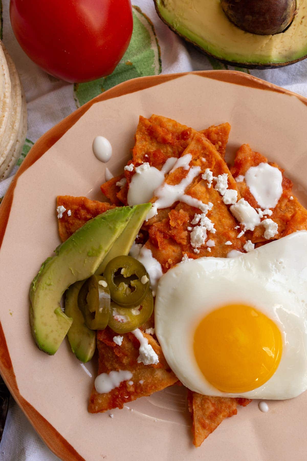 Closeup of a retro plate of red chilaquiles with sliced avocado, crumbled cheese, and fried egg.