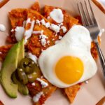 Closeup of a retro plate of red chilaquiles with avocado and fried egg on top.