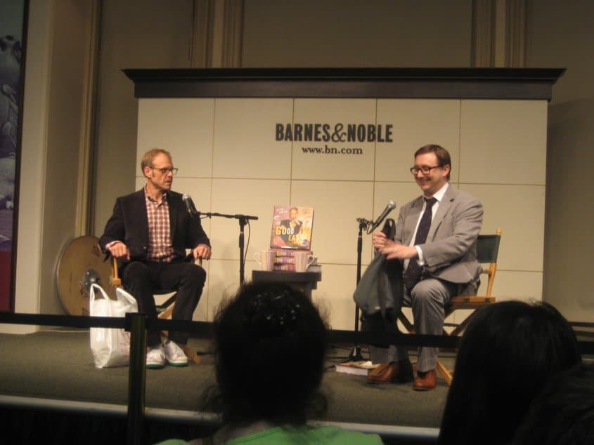 two men with microphones sitting on a stage