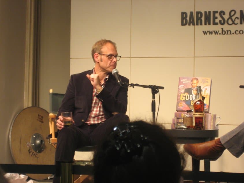 Alton Brown sitting in a chair and talking into a microphone