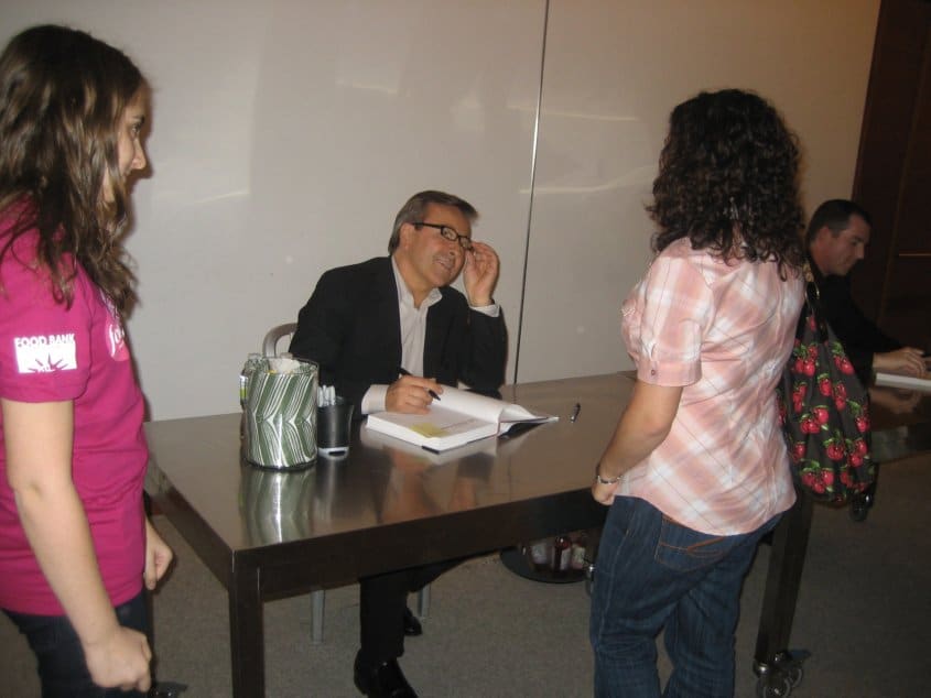 Daniel Boulud sitting at a table talking to a woman standing across from him