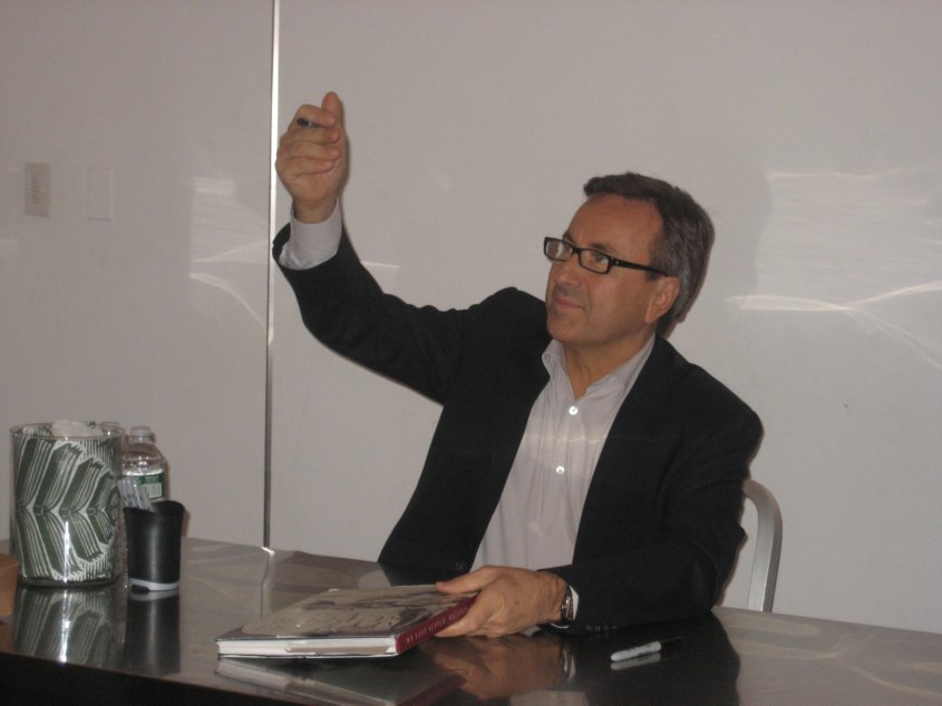 Daniel Boulud sitting at a table and raising his hand