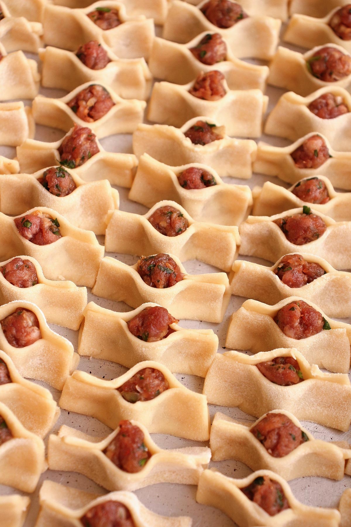 Uncooked Armenian manti arranged in tight rows in a metal pan.