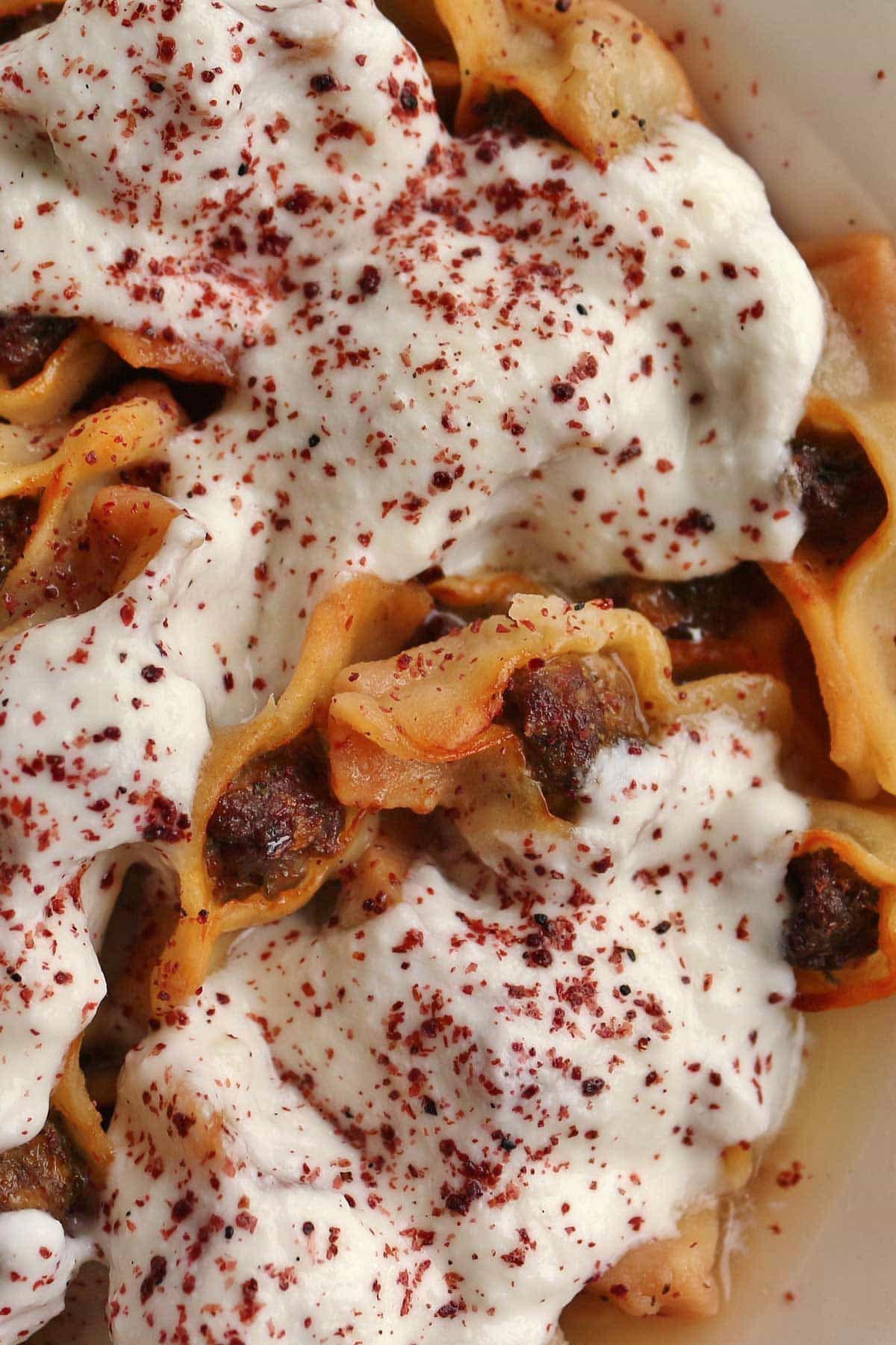 Closeup of canoe-shaped manti dumplings topped with yogurt sauce and ground sumac.