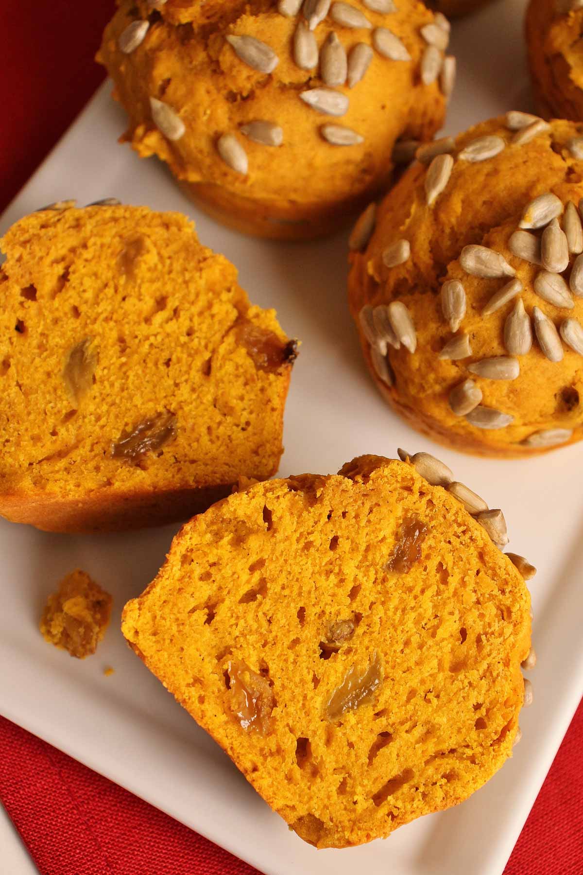 Pumpkin muffins on a white plate with one cut in half to show golden raisins inside.