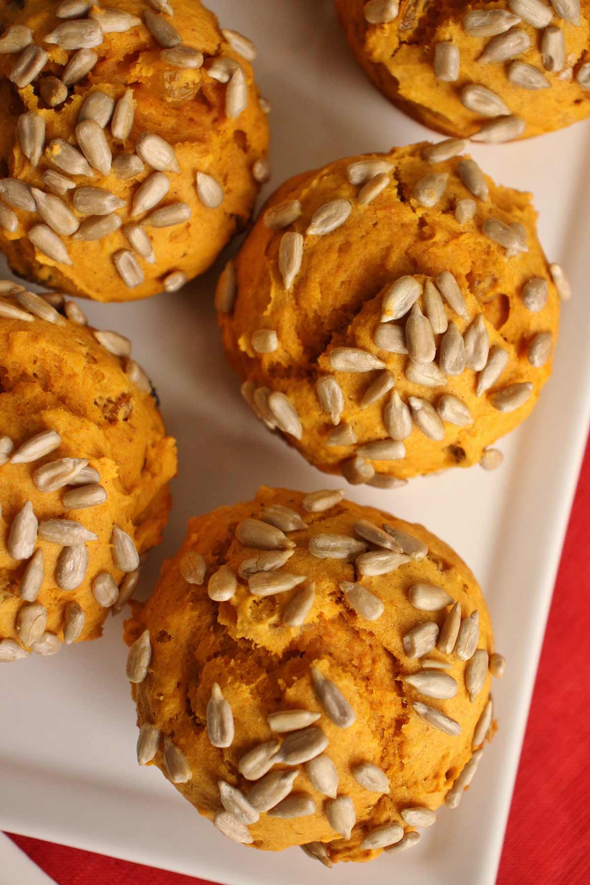 Orange-hued pumpkin muffins topped with sunflower seeds on a white rectangular dish.