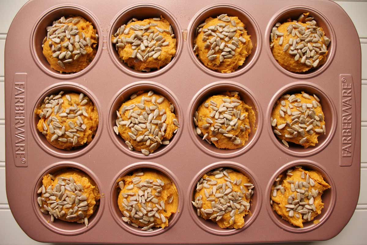 Bright orange batter divided up in a pink muffin pan.