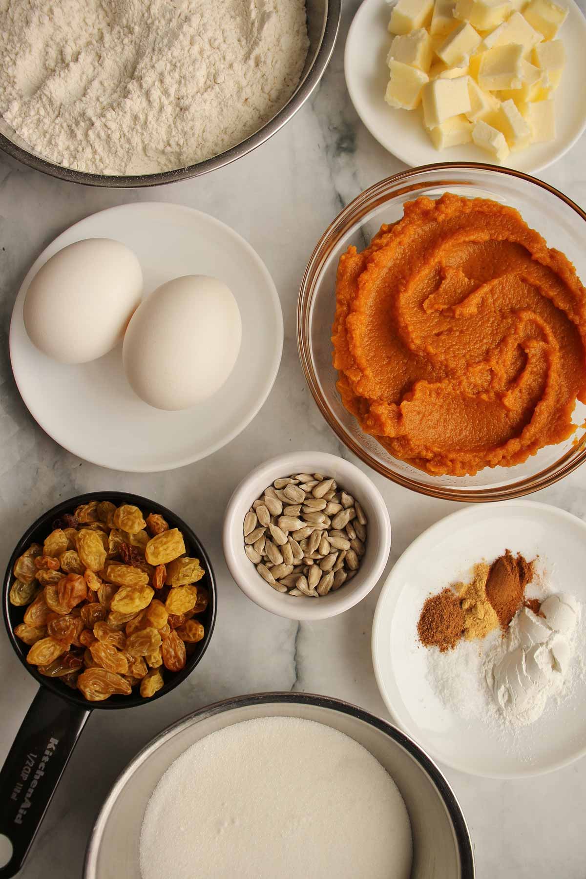 Ingredients for pumpkin raisin muffins including eggs, butter, pumpkin puree, sugar, flour, and spices.