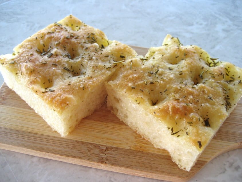 a closeup of two squares of focaccia bread on a small wooden board