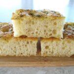 closeup side view of three squares of focaccia bread on a small wooden board