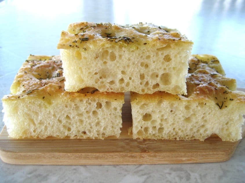 closeup side view of three squares of focaccia bread on a small wooden board