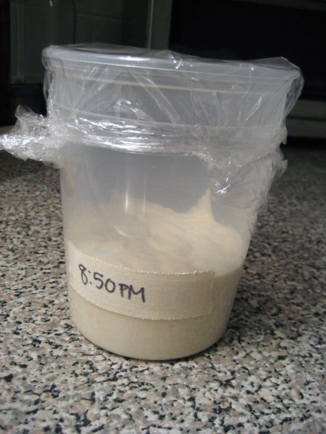 a plastic quart container filled with bread starter with a piece of tape labeling the time