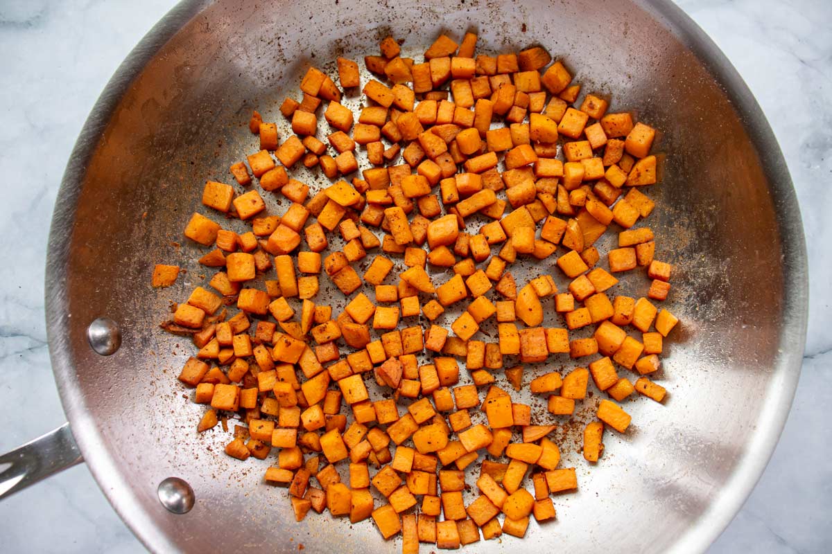 Cooked cubed sweet potato in a metal skillet.