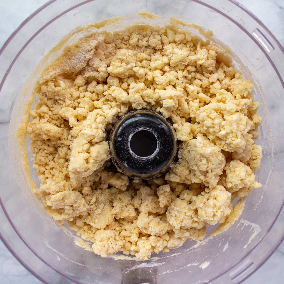 Crumbly dough mixture in a food processor bowl.