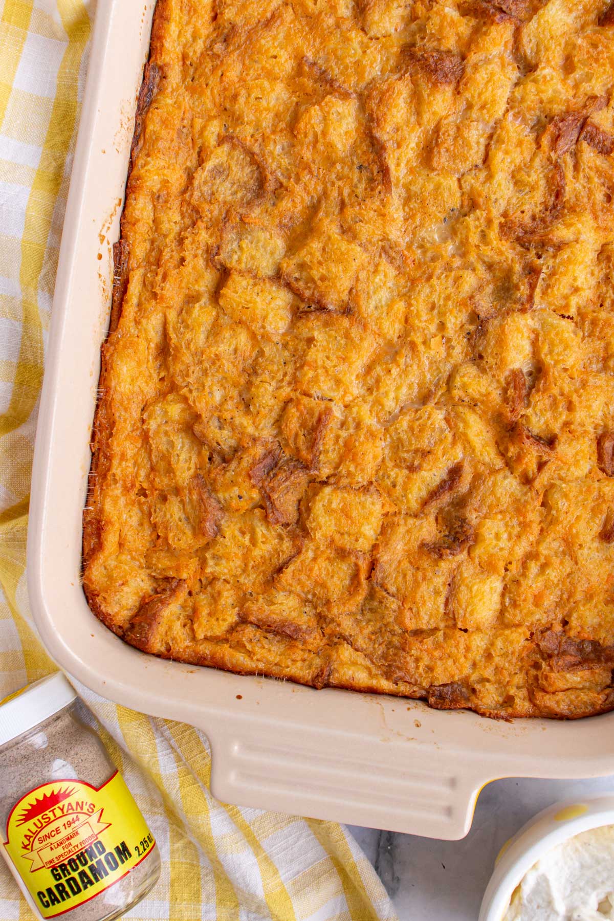 Sweet potato bread pudding in a casserole dish next to a small jar of ground cardamom.