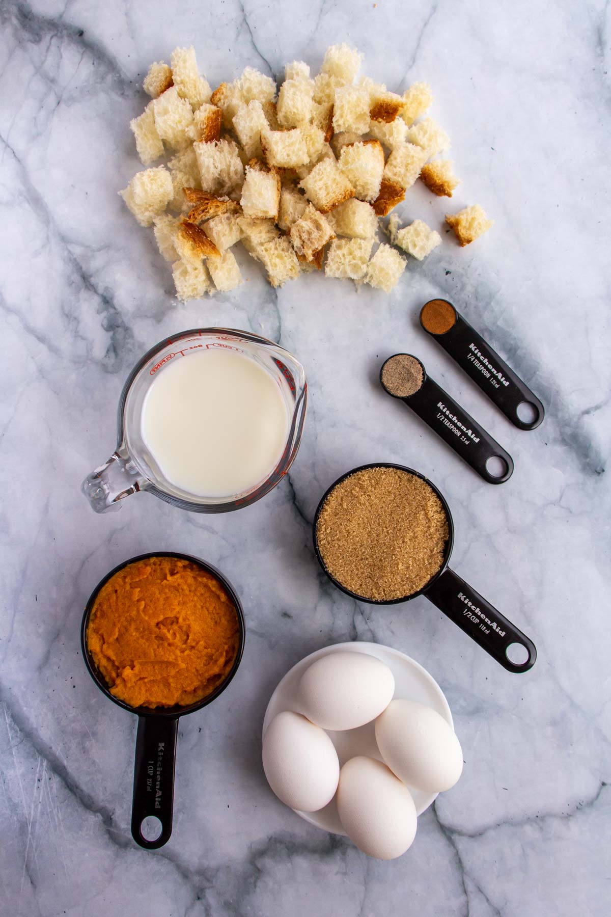 Ingredients for sweet potato bread pudding on a white marble background.