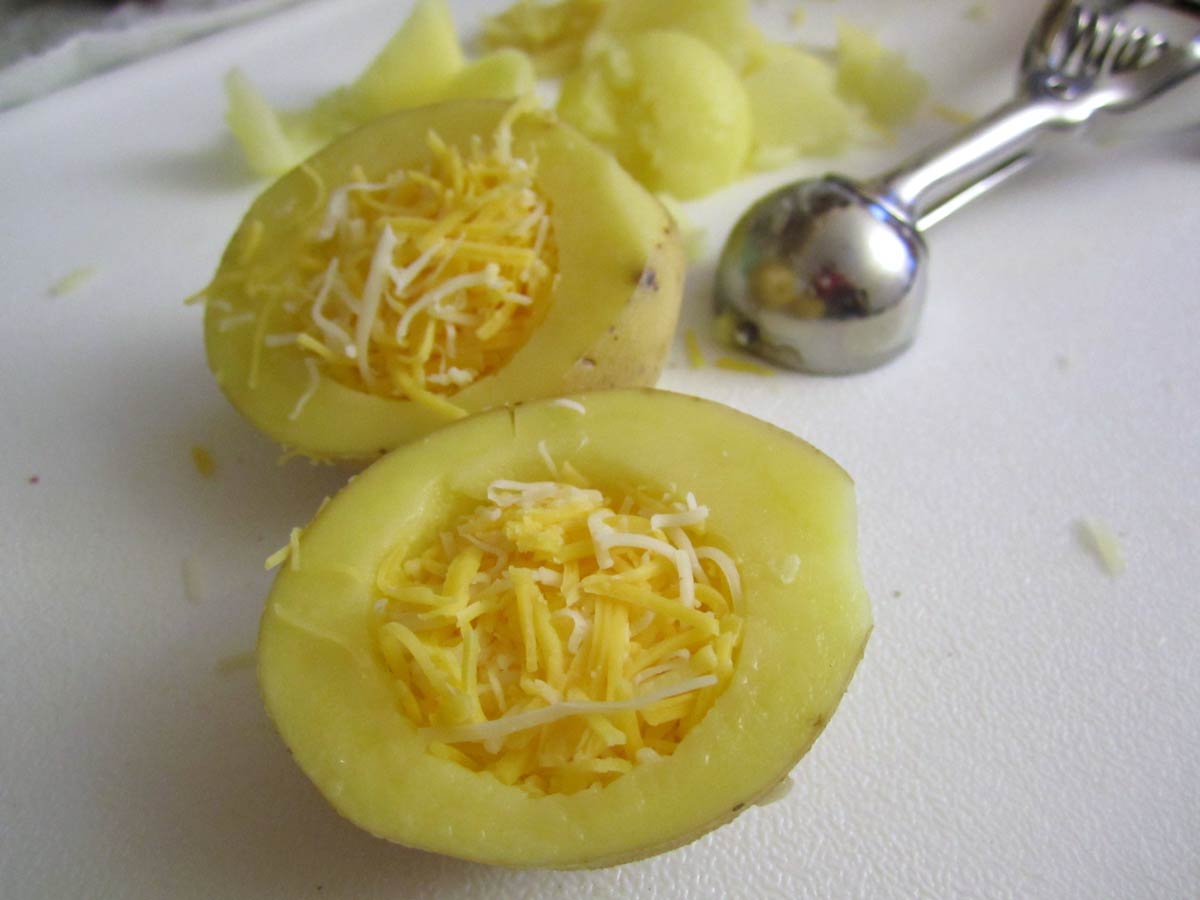 A potato cut in half with the middle scooped out and filled with shredded cheese.