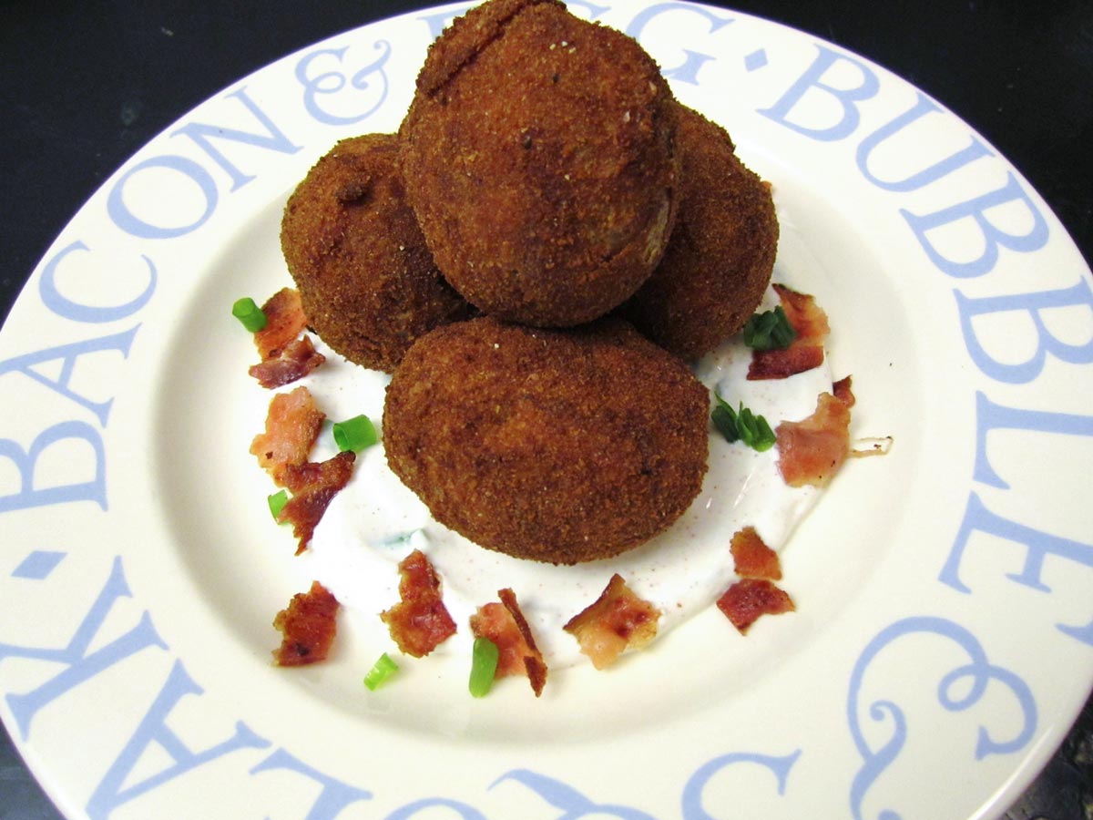 A pile of breaded fried small potatoes with bacon and scallions around it.