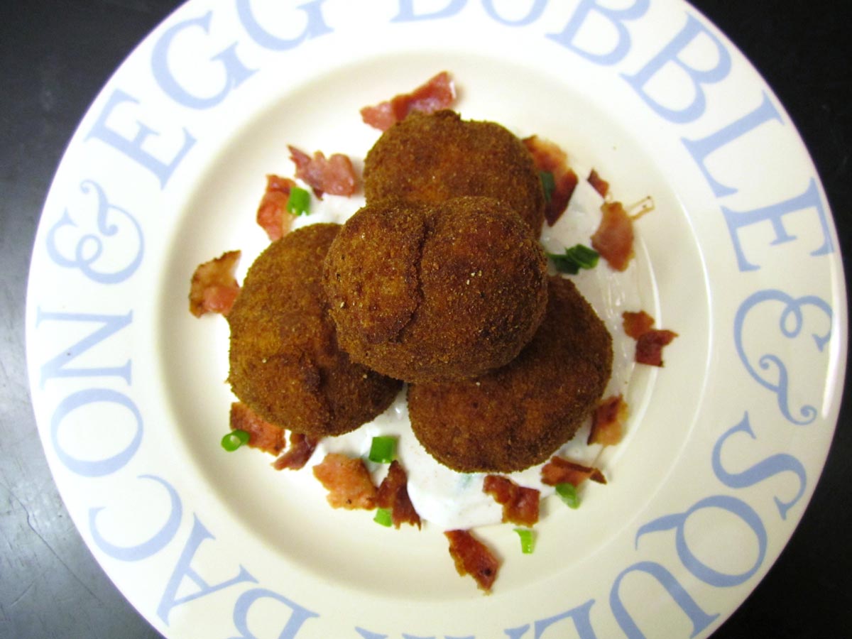 A pile of breaded fried potatoes with bacon and scallions.