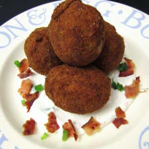 A pile of breaded fried small potatoes with bacon and scallions around it.