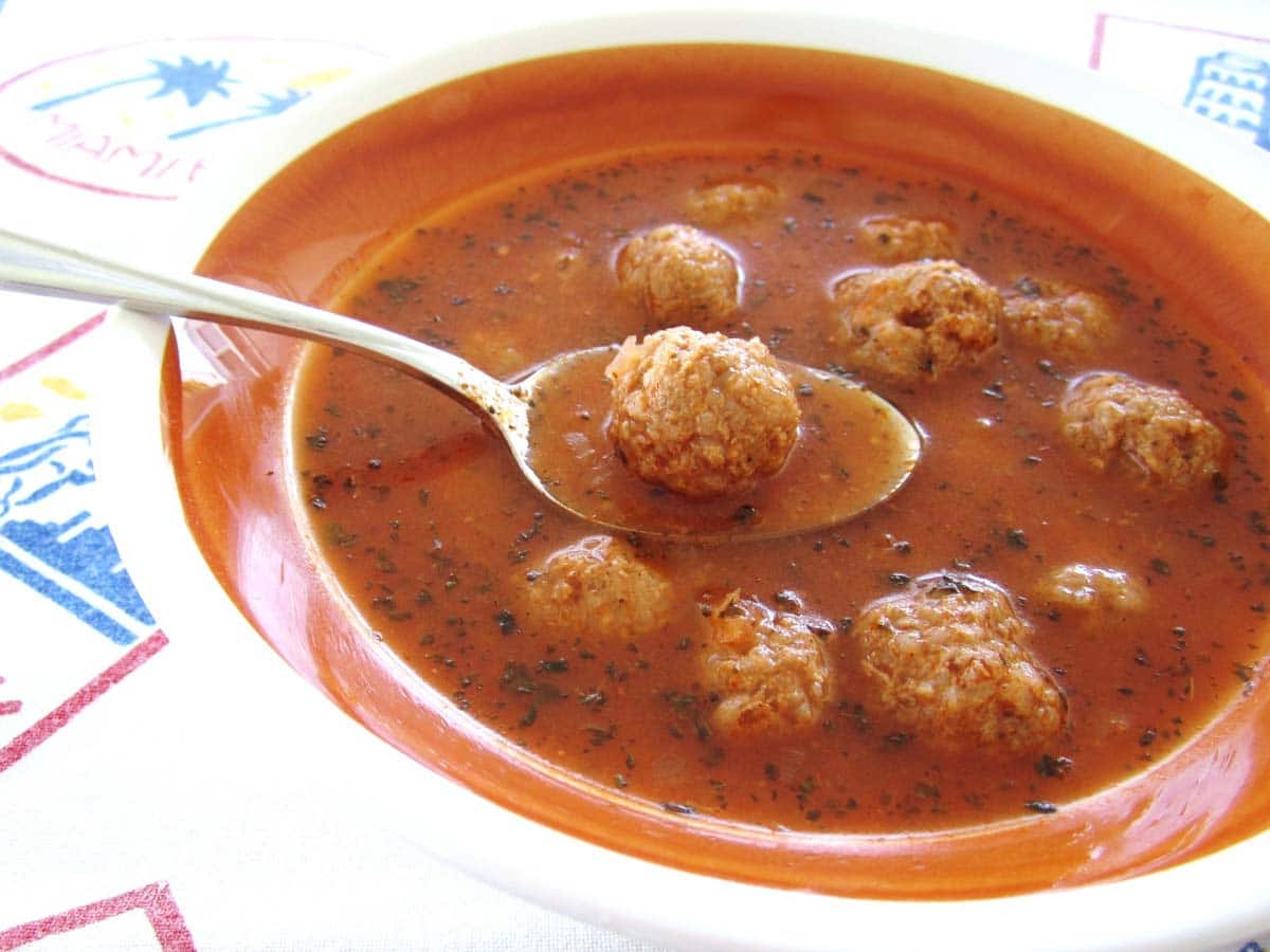 A spoon is lifting a meatball out of the bowl of Armenian meatball soup.