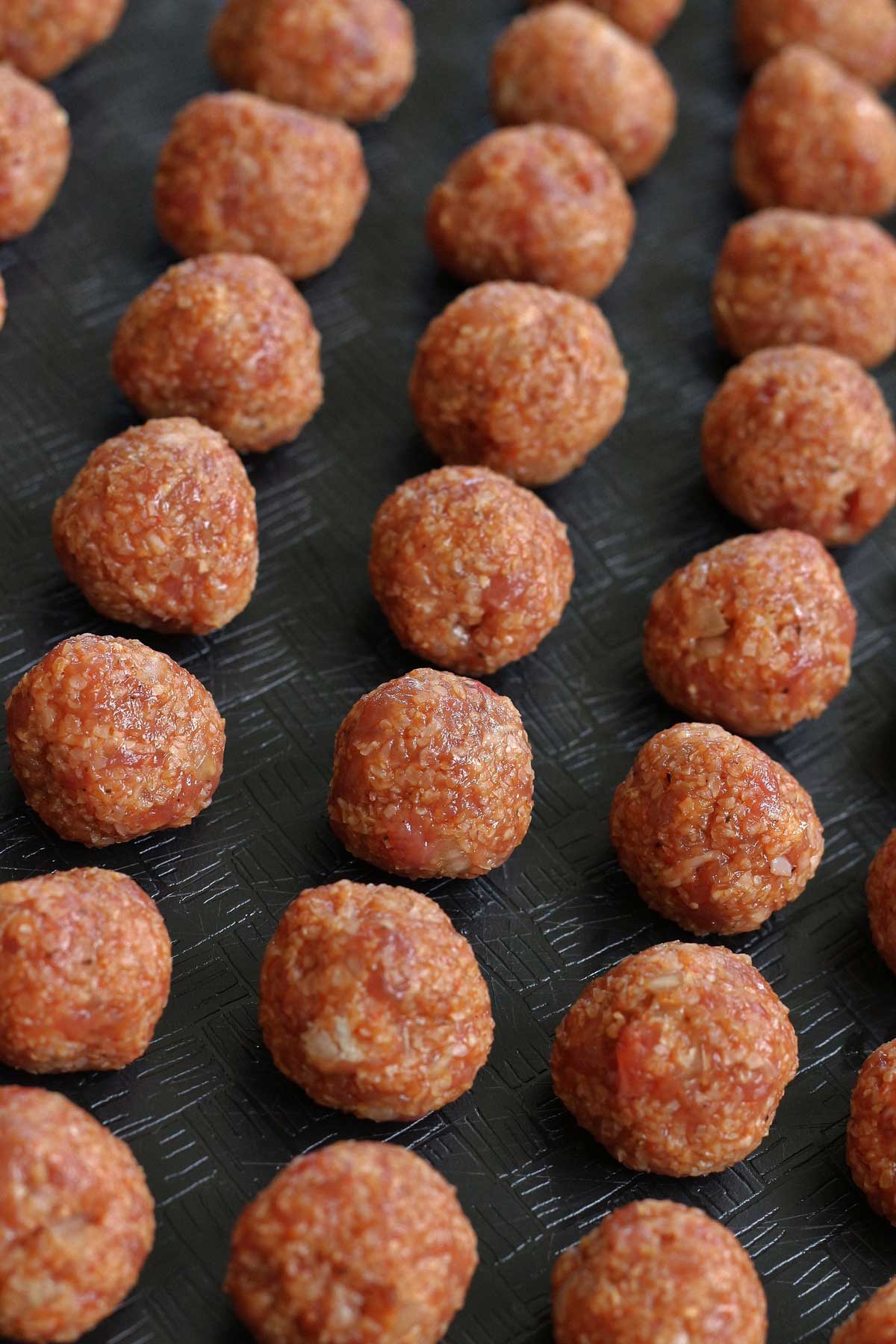 A closeup of small beef and bulgur meatballs on a black surface.