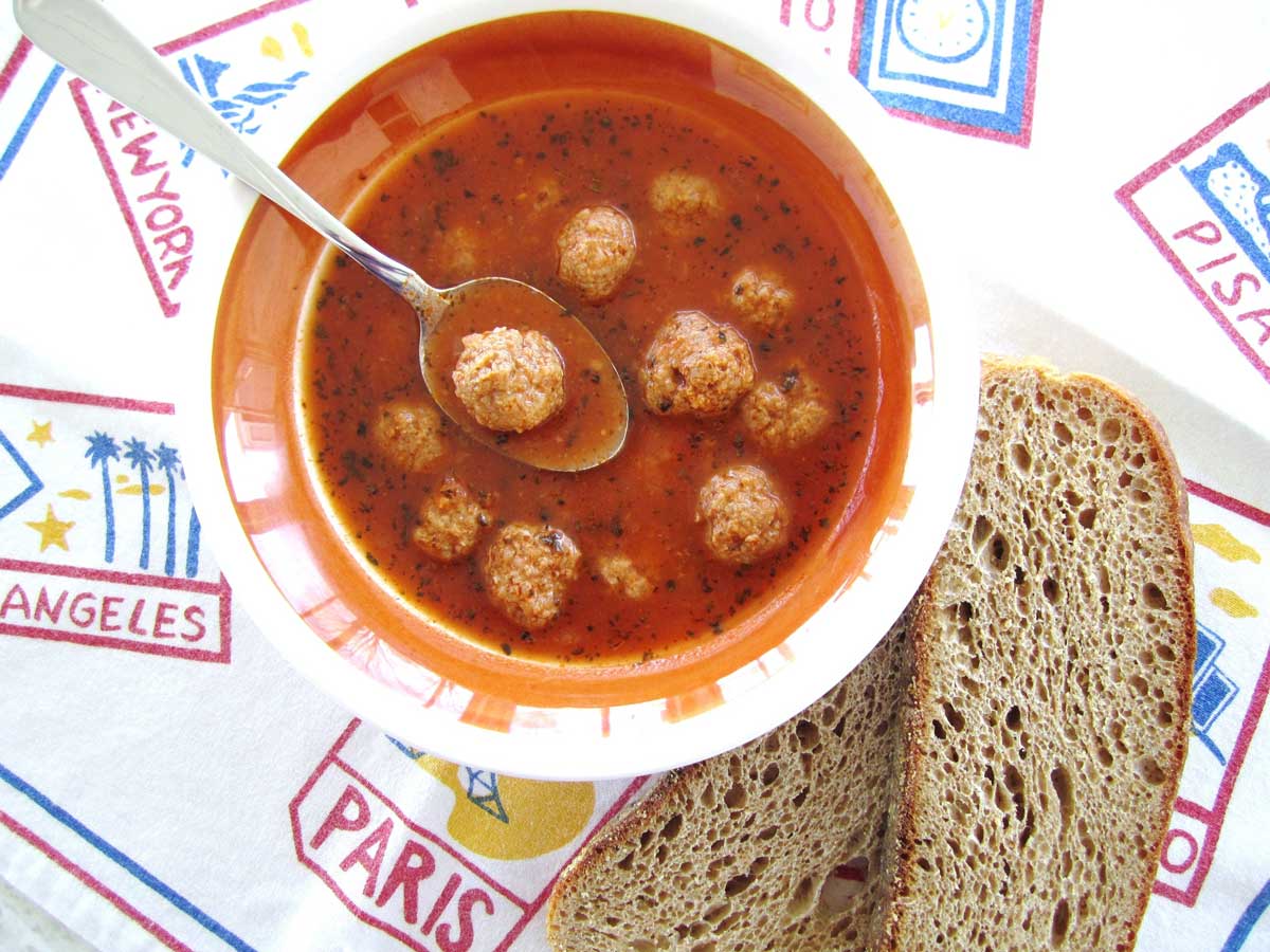 A bowl of Armenian meatball soup with sliced wheat toast next to the bowl.