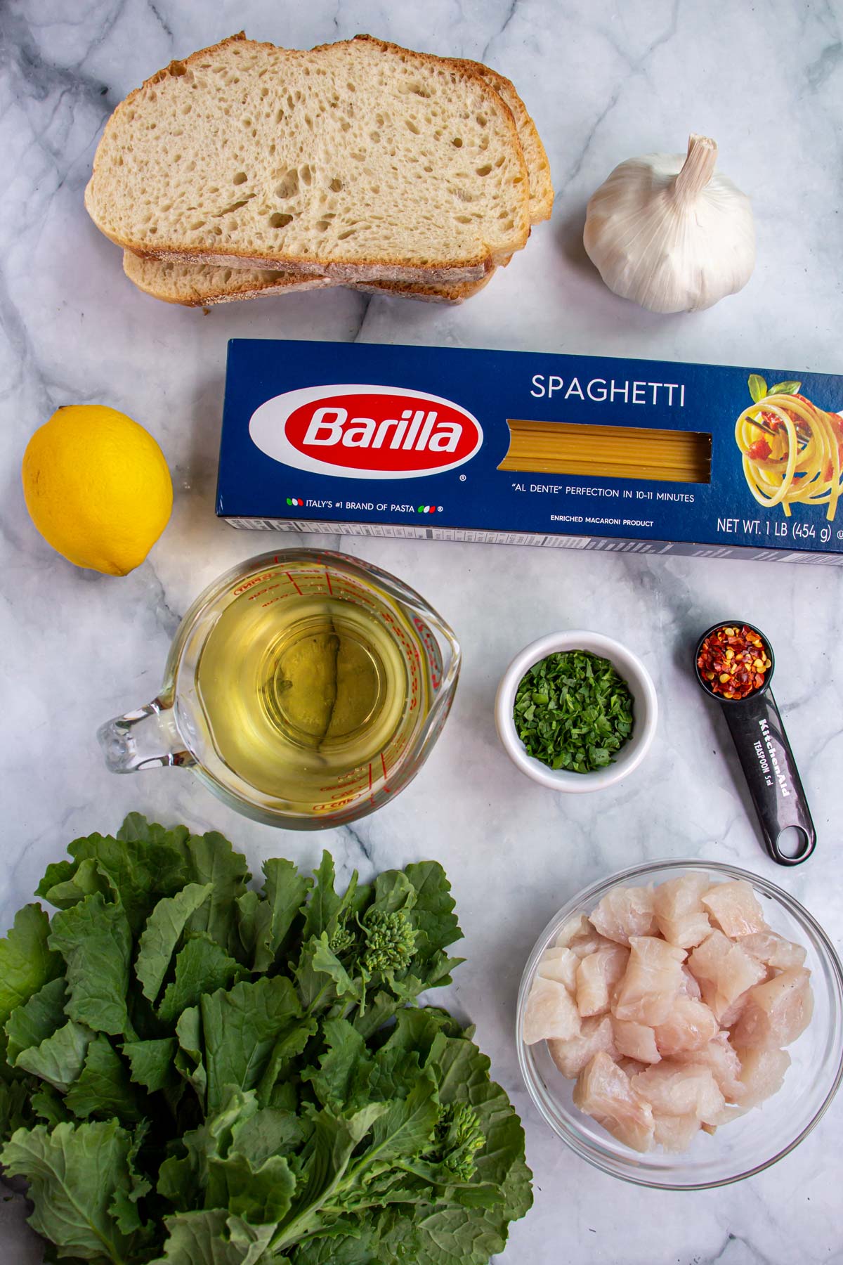 Ingredients for spaghetti with cod, rapini and breadcrumbs on a white marble background.