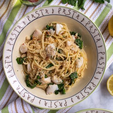A bowl of spaghetti with broccoli rabe, small pieces of cod, and breadcrumbs on top.
