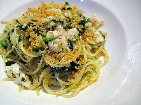 spaghetti with flaked cod, rapini and breadcrumbs on top on a white plate