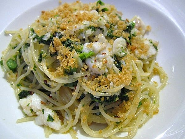 A closeup of spaghetti with flaked cod, broccoli rabe, and bread crumbs on a white plate