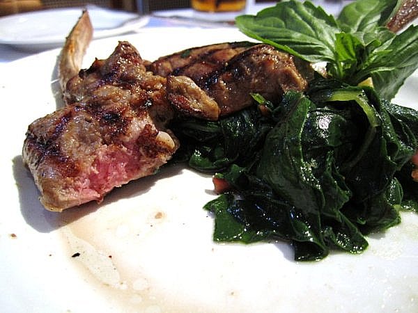 a half-eaten lamb chop with Swiss chard on a white plate