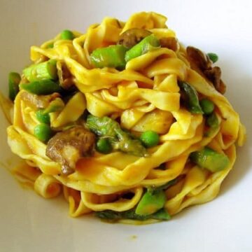an elegant pile of fettuccine in bright yellow sauce with peas, chopped asparagus, and mushrooms