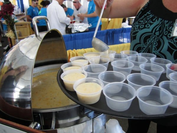 someone with a ladle pouring samples of chowder into small plastic cups on a tray