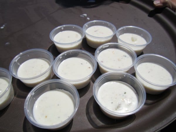 a black tray topped with small plastic cups filled with white chowder samples