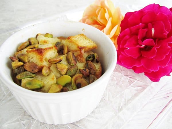 a closeup of a ramekin of bread pudding with pistachios with two roses in the background