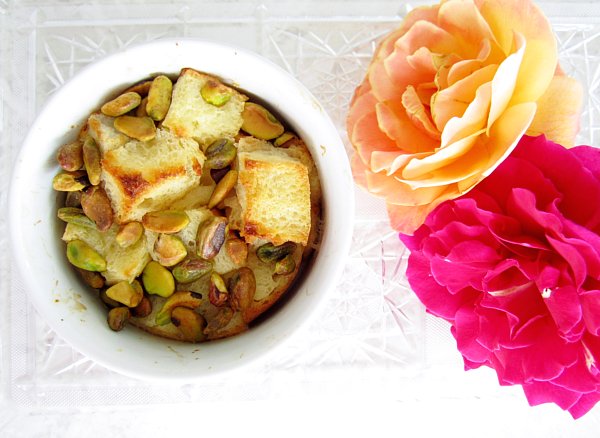 overhead closeup of bread pudding with pistachios in a ramekin next to colorful roses