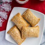 Four sesame seed topped rectangular Chinese pastries on a square white plate.