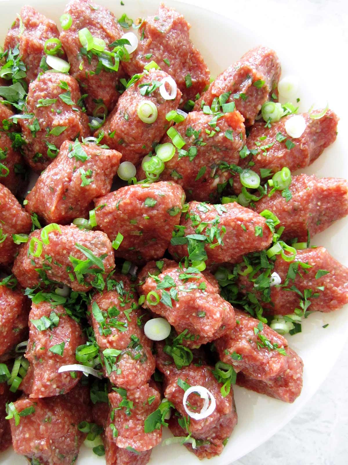 Closeup of a platter of chi kofte topped with chopped parsley and scallions.