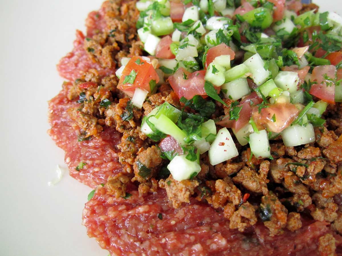 Closeup of chi kofte flattened on a plate garnished with gheyma (ground beef) and salad.