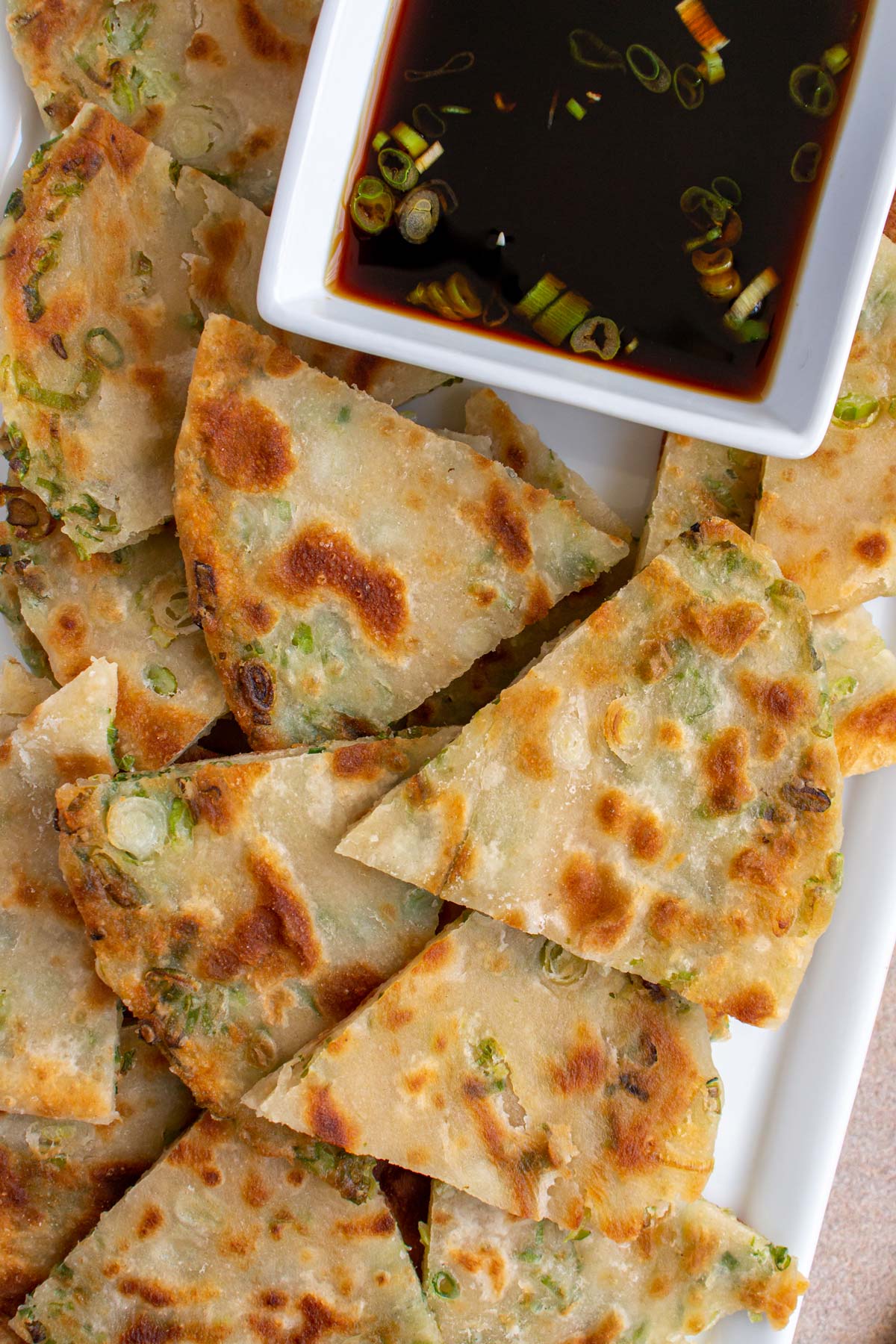 Closeup of a platter of Chinese scallion pancake triangles with soy dipping sauce.